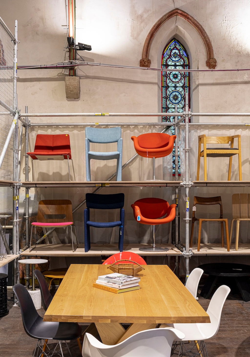 Colorful chairs arranged on metal shelves with a stained glass window in the background.